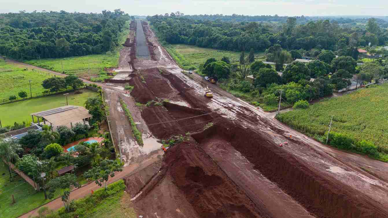 Vista aérea de terraplenagem de uma via em obras, cercada por mata e lavoura
