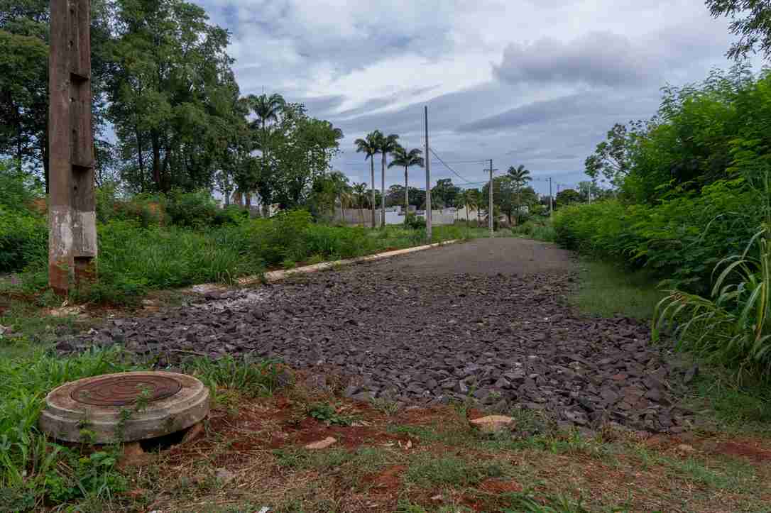 Trecho de via sem pavimentação, com pedras soltas e mato nas laterais